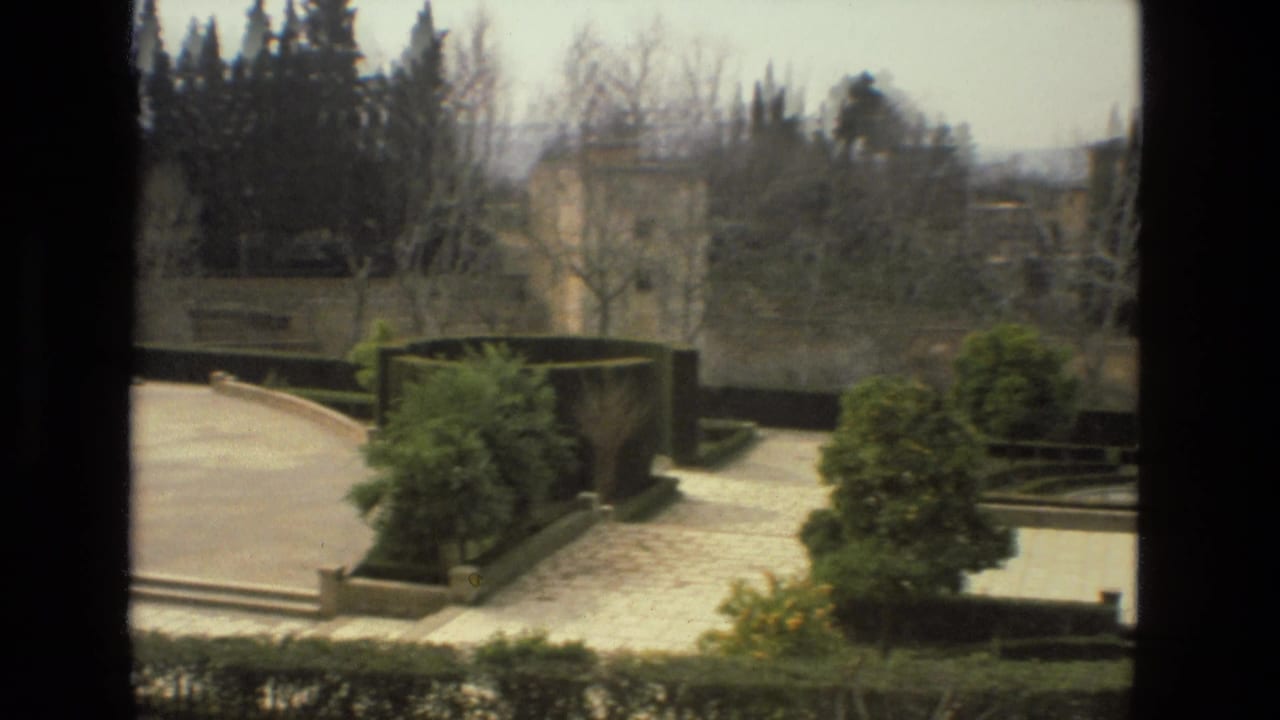 Elevated view of terraced garden paths with hedges, trees, and pale stone walkways.