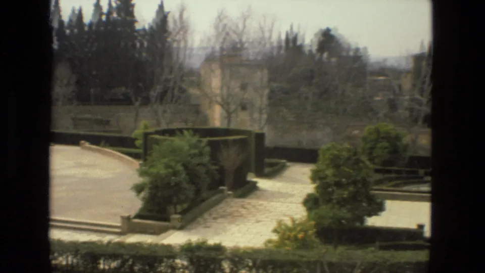1978 8mm view in Córdoba, Spain, looking over a landscaped garden with curved stone paths, hedges, and tall trees.