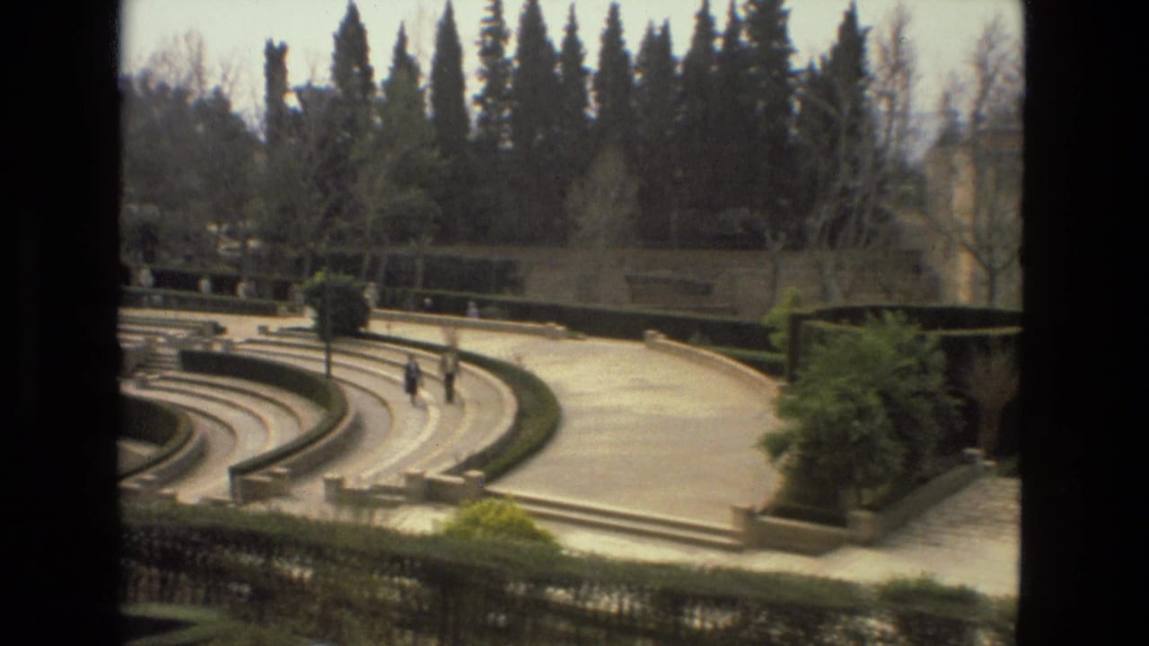 Curved amphitheater-like garden steps with hedges, cypress trees, and small distant visitors.