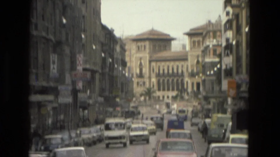 1978 Córdoba street view with classic cars, pedestrians, tall facades, and a prominent arched-window building in the distance.