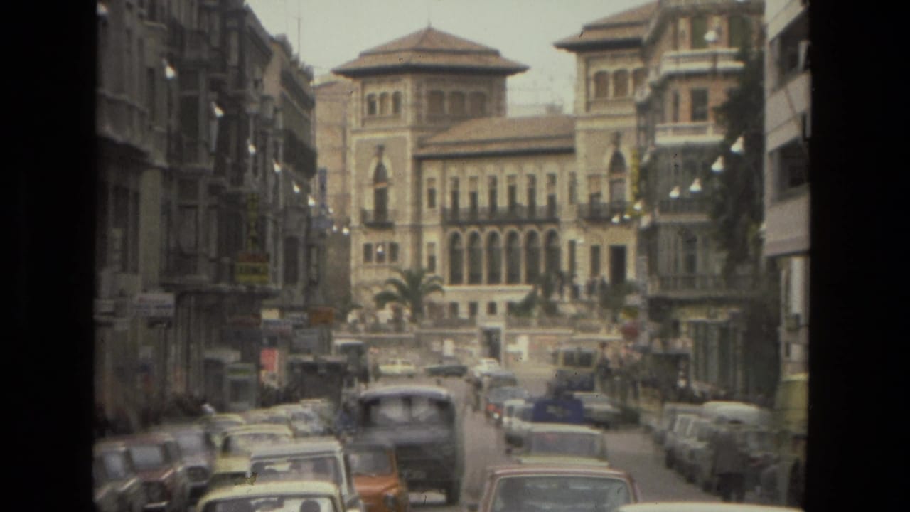 Narrow city street with cars, pedestrians, and a large arched building ahead.