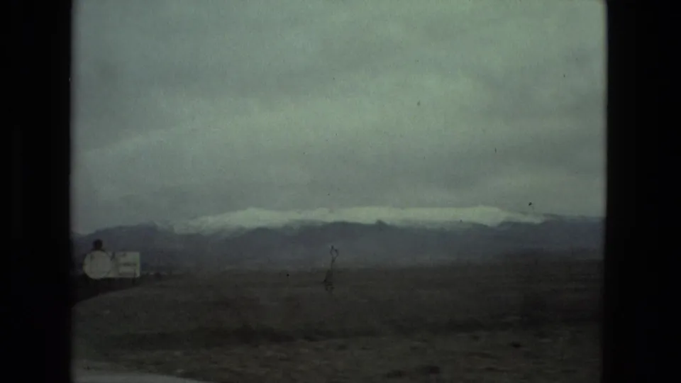 1978 8mm travel frame near Seville, Spain, looking across a dry roadside plain toward a dark mountain ridge with snow on top.