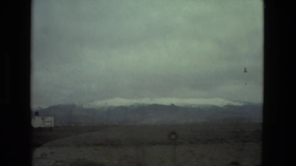End frame of a 1978 8mm vehicle view near Seville, Spain, with open land, roadside markers, and snow-capped mountains under overcast light.