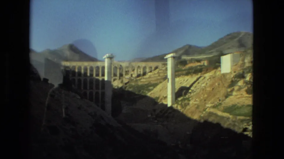 1978 8mm frame showing a large arched bridge or aqueduct-like structure among rocky hills near Seville, Spain.