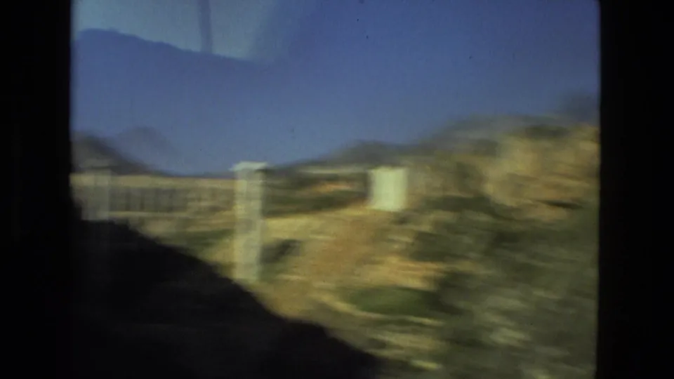 Motion-blurred 1978 8mm frame of the arched bridge or aqueduct-like structure against hills and blue sky near Seville, Spain.