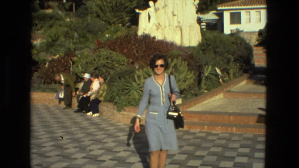 Seville, Spain, 1978 frame showing the woman closer to camera, carrying a black handbag beside a landscaped garden and monument.