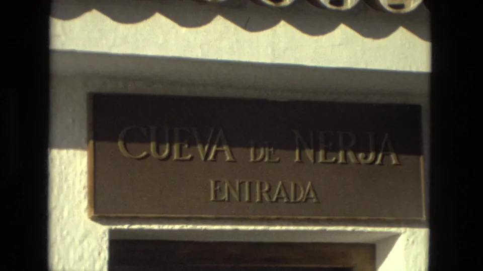A 1978 home-movie close-up shows the Cueva de Nerja Entrada sign mounted on a white stucco wall in bright sunlight.