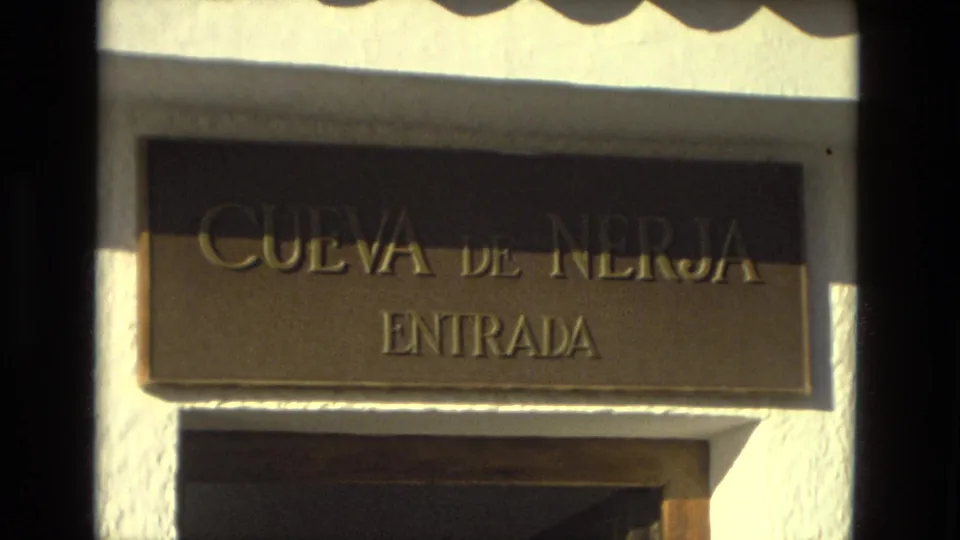 The Cueva de Nerja Entrada sign appears above a doorway, filmed in warm 8mm color with strong sun and slight handheld framing.