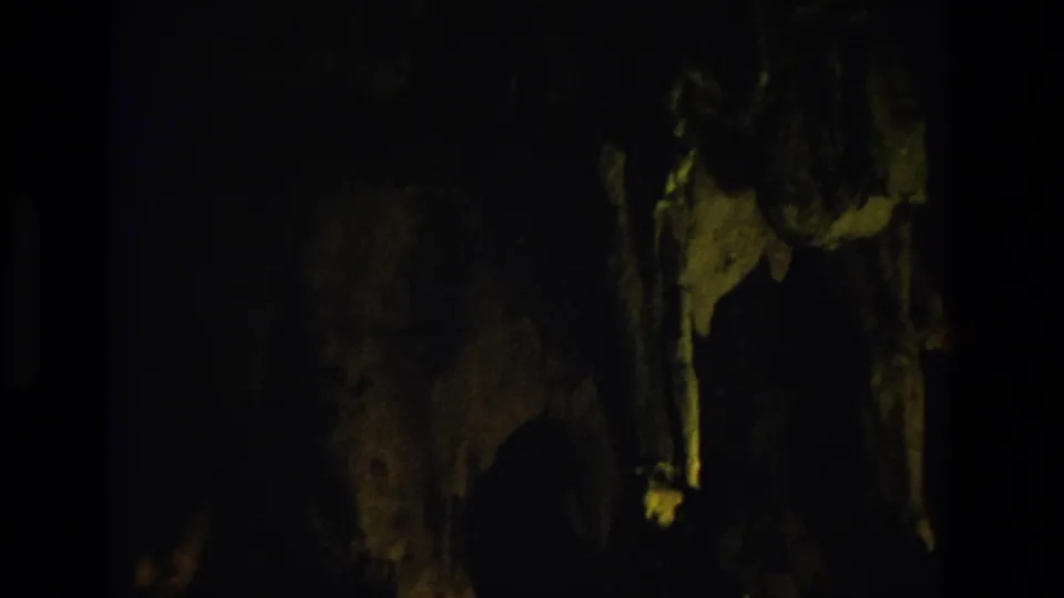 Inside the cave, dim 8mm footage shows shadowed rock formations with small patches of light and pronounced grain.