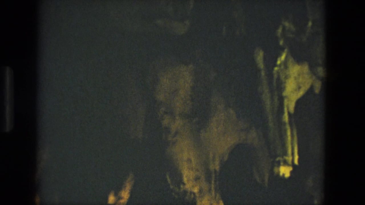 Dim cave wall with yellow-green highlights and dark film borders.