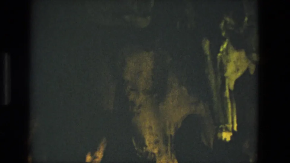 1978 8mm frame from Seville showing a dark rocky cave surface with yellow-green illumination and heavy shadow.