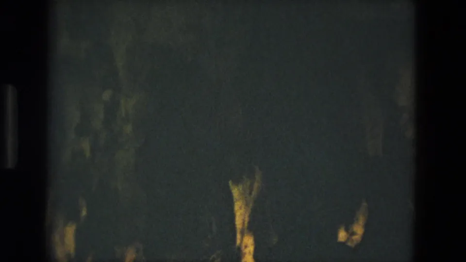 Low-light 8mm cave view from the Seville clip, with rough rock shapes barely visible under yellow-green light.