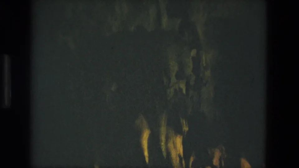 1978 Seville home-movie frame showing a very dark cave wall, blurred rock texture, and yellow-green light on uneven surfaces.