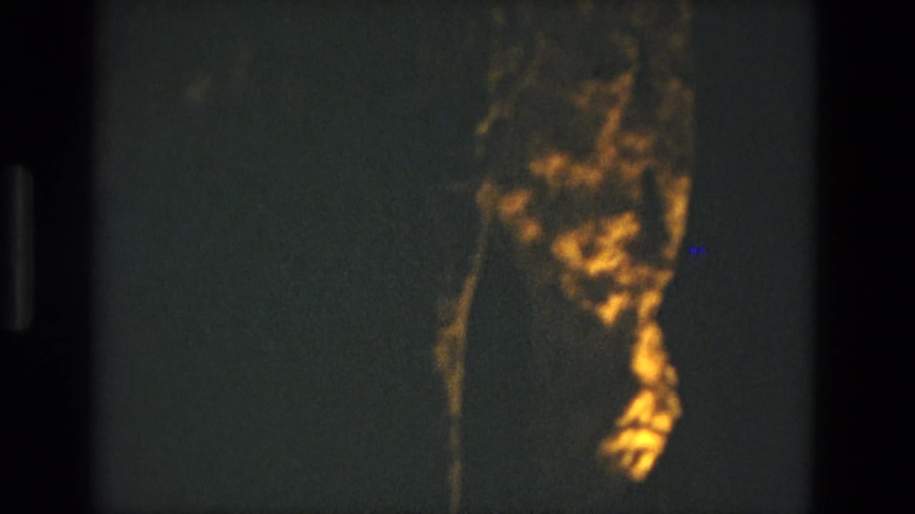 1978 8mm frame from Seville, Spain showing a dim cave interior with a golden-lit rock formation against dark stone.