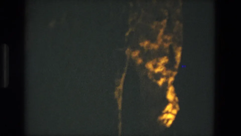 1978 8mm frame from Seville, Spain showing a dim cave interior with a golden-lit rock formation against dark stone.