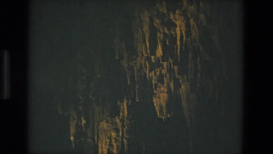 1978 8mm frame from Seville, Spain showing shadowed cave rock with vertical formations picked out by warm illumination.