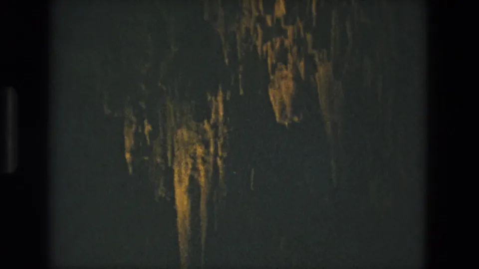 1978 8mm frame from Seville, Spain showing clustered cave formations glowing in warm light inside a dark cavern.