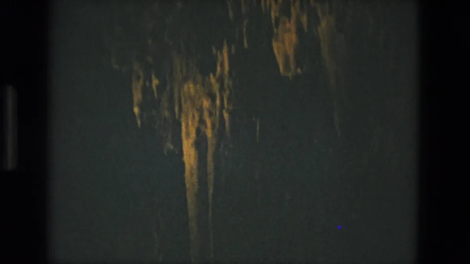 1978 8mm frame from Seville, Spain showing a narrow warm-lit cave formation dropping through a shadowed interior.