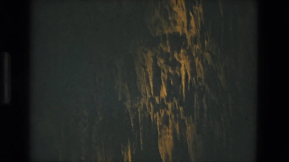 1978 Seville 8mm frame showing a shadowed passage surface with golden streaks, heavy grain, and dark film-gate edges.