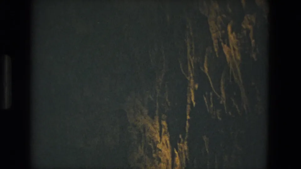 1978 Seville 8mm frame with a dim textured wall, amber reflected light, and a prominent dark vertical film edge.