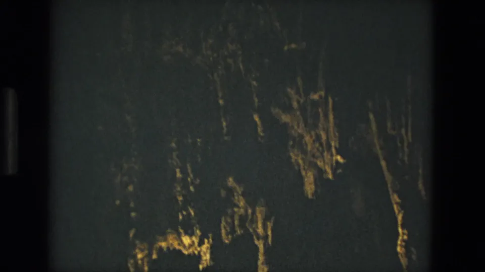 1978 Seville 8mm frame showing a dark lower passage or wall area with scattered gold highlights and dense grain.