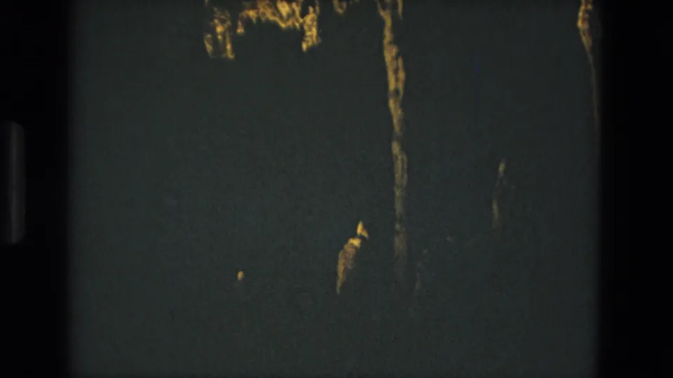 1978 Seville 8mm frame with a mostly dark wall or tunnel surface, thin golden streaks, and underexposed film texture.