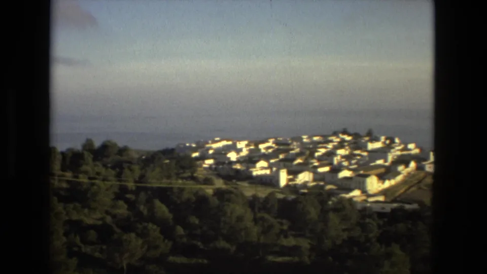 1978 8mm frame showing a compact white town on rising ground, with trees below and hazy water behind it.