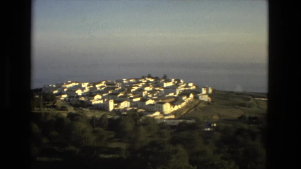 1978 8mm view of the white hillside settlement, terraced land, and open water under a soft hazy sky.