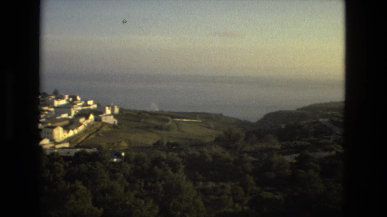 1978 Spanish 8mm view of white hillside buildings, green terrain, and distant sea seen through dark framing.