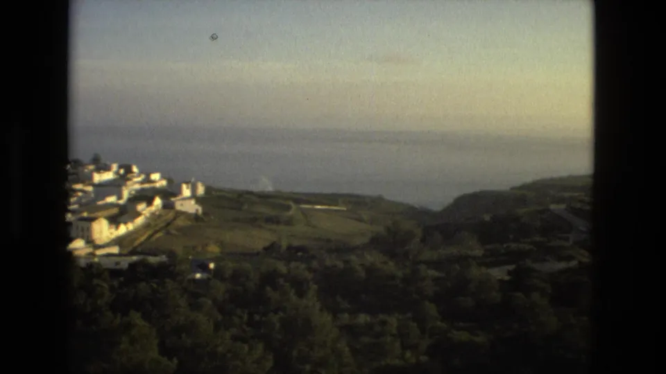1978 Spanish 8mm view of white hillside buildings, green terrain, and distant sea seen through dark framing.