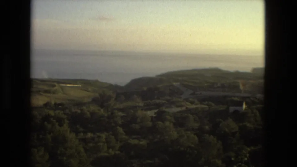 1978 Spanish home-movie frame showing coastal hills, open sea, roads, and vegetation under a hazy sky.