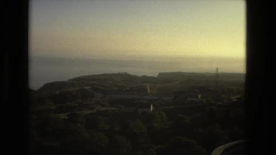 Soft 8mm frame of a Spanish coastline with headland, sea, trees, and dark window-like edges.