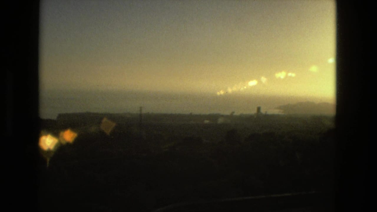 Soft sunset view through dark film-frame borders with distant land and water.