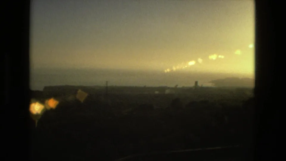 1978 8mm frame showing a hazy sunset or flare over a distant landscape and water, with dark contact-sheet borders.