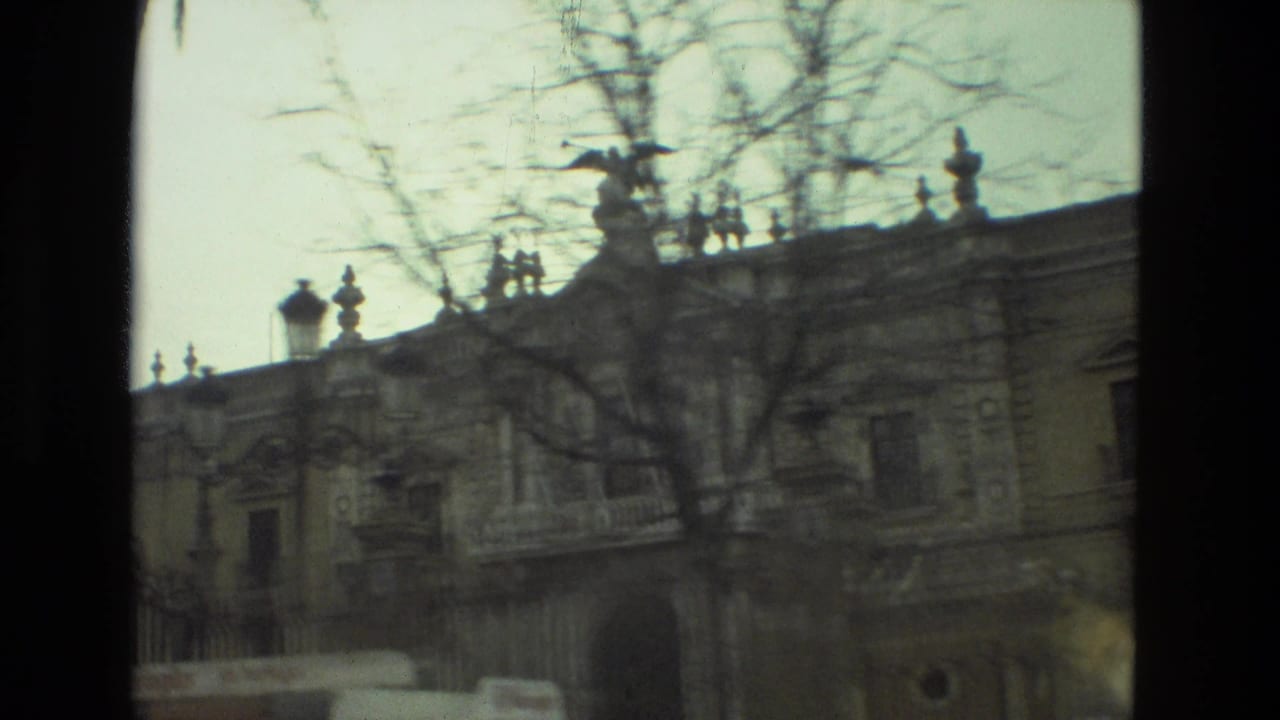 1978 Seville 8mm frame showing a historic stone facade behind bare branches, with lamps and roofline details visible.