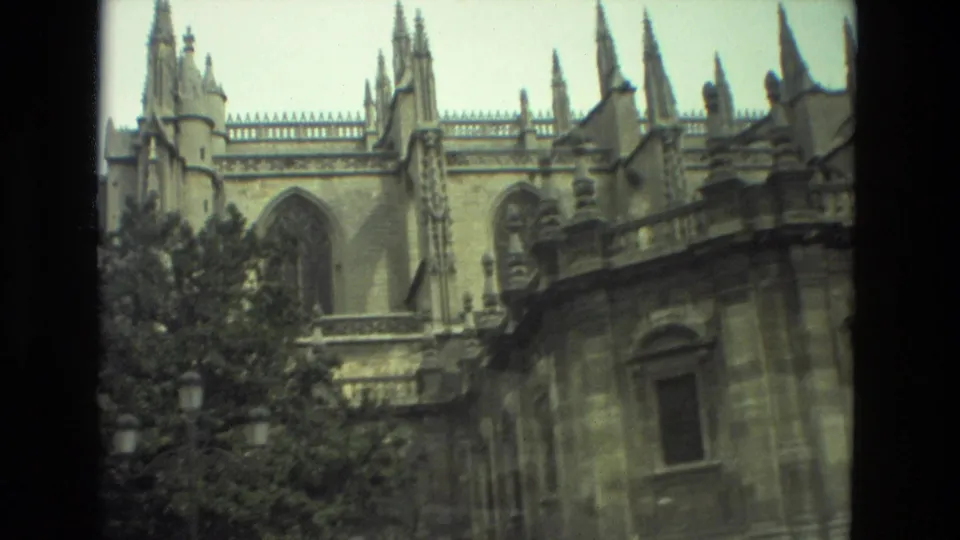 1978 Seville frame with pointed Gothic-style spires, arched stonework, trees, and a lower historic wall.