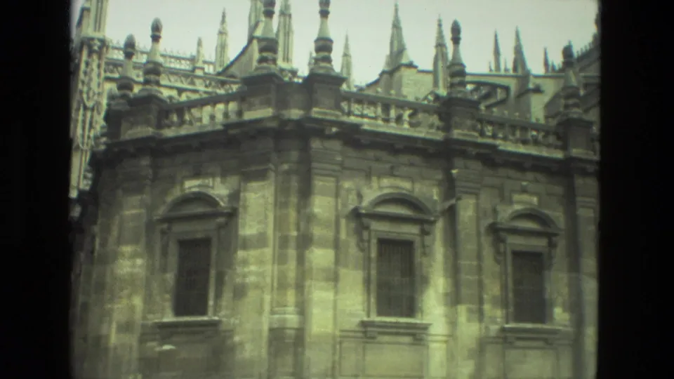 1978 Seville 8mm view of an ornate stone facade with tall framed windows, parapet details, and spires behind.