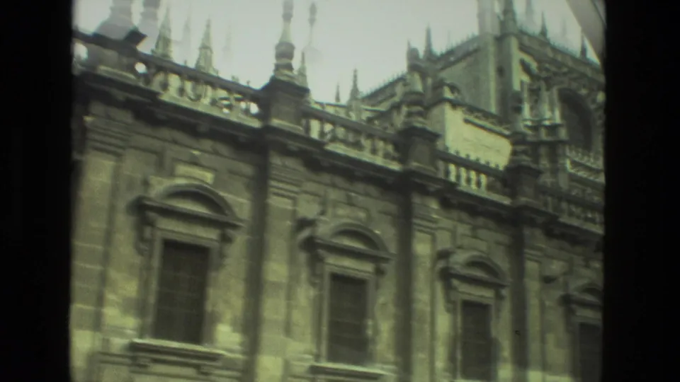 1978 Seville frame showing a long stone exterior with arched windows, parapet details, and spires beyond the roofline.