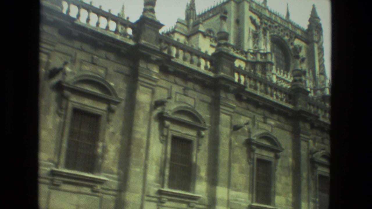 1978 8mm home-movie view in Seville showing an ornate stone exterior with arched windows, carved panels, and roofline spires.