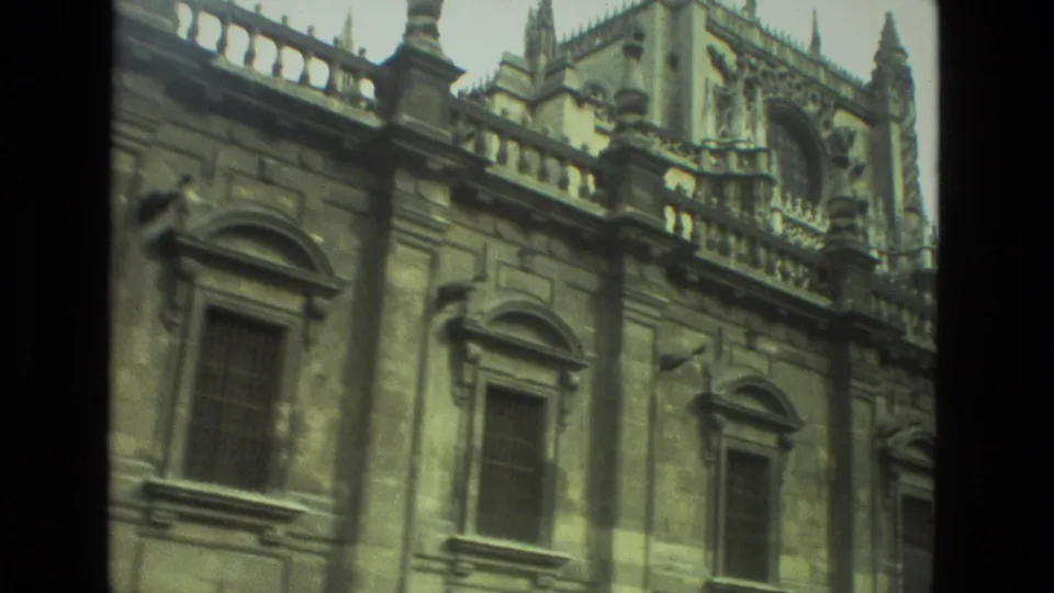 1978 8mm home-movie view in Seville showing an ornate stone exterior with arched windows, carved panels, and roofline spires.