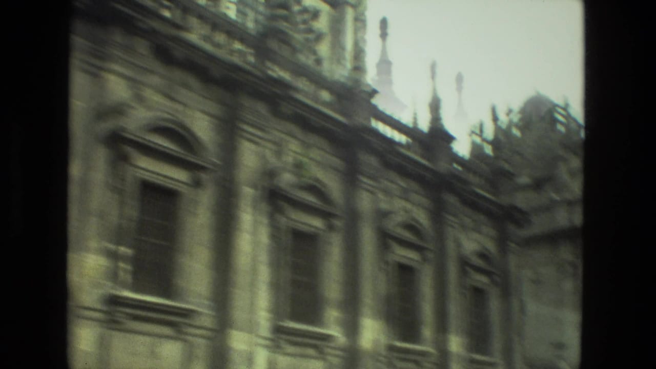 1978 Seville travel footage frames a historic stone wall with tall arched windows, carved trim, and blurred roofline ornament.