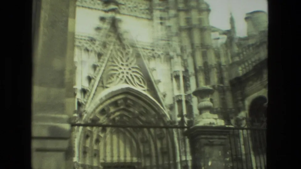 1978 Seville home-movie frame showing a pointed Gothic-style entrance detail behind iron fencing, with carved stonework and vertical columns.