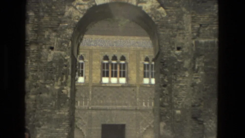 Seville 1978 home-movie frame with a rough stone arch framing decorated windows and a doorway inside the courtyard.
