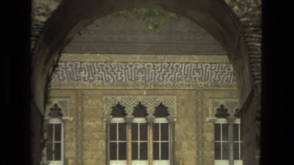 1978 8mm Seville view of an ornate facade with arched windows, carved trim, and a blue tile inscription framed by shadowed architecture.