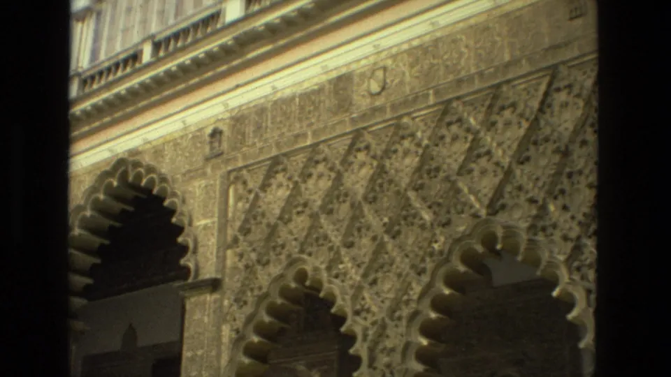 1978 8mm Seville facade detail with scalloped arch openings, patterned carved panels, and upper stone trim in warm light.