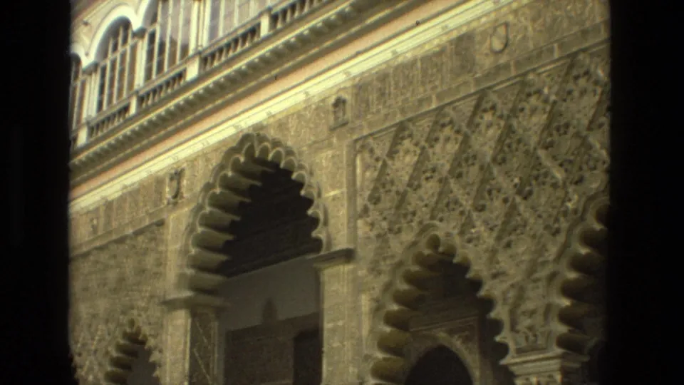 1978 Seville home-movie frame of an ornate exterior wall with scalloped arches, carved geometric panels, and an upper arched window.