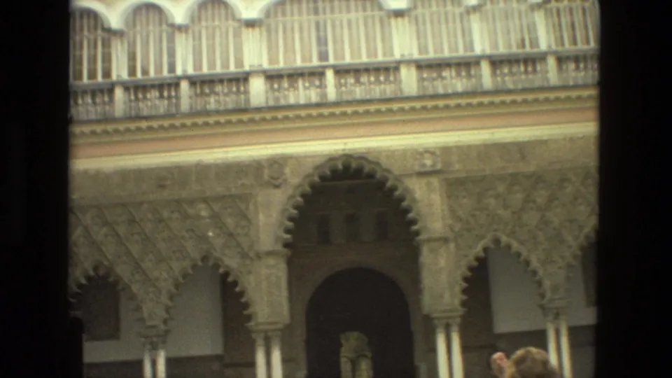Final Seville frame with carved arches, upper balcony windows, and distant tourists partly visible at the base of the architecture.