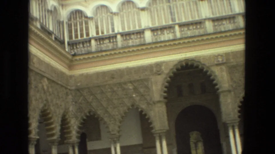 1978 Seville home-movie frame showing Moorish-style courtyard arches, carved wall surfaces, columns, and an upper gallery.