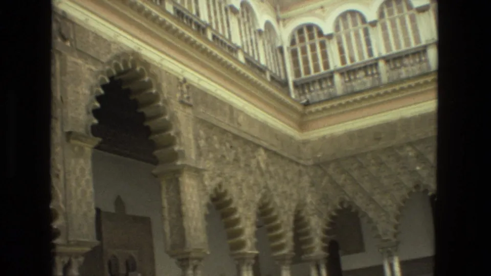 1978 Seville frame with a tall scalloped arch, patterned wall surfaces, columns, and upper-level railings in a historic courtyard.