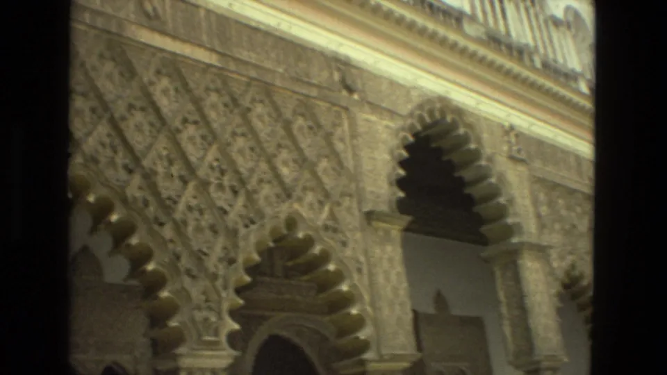 1978 Seville home-movie frame looking upward across carved Moorish-style arches, columns, and decorative wall surfaces.